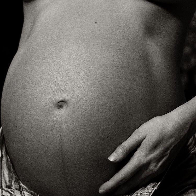 Pregnant woman gently holding her belly while preparing for a supported postpartum and fourth trimester.”