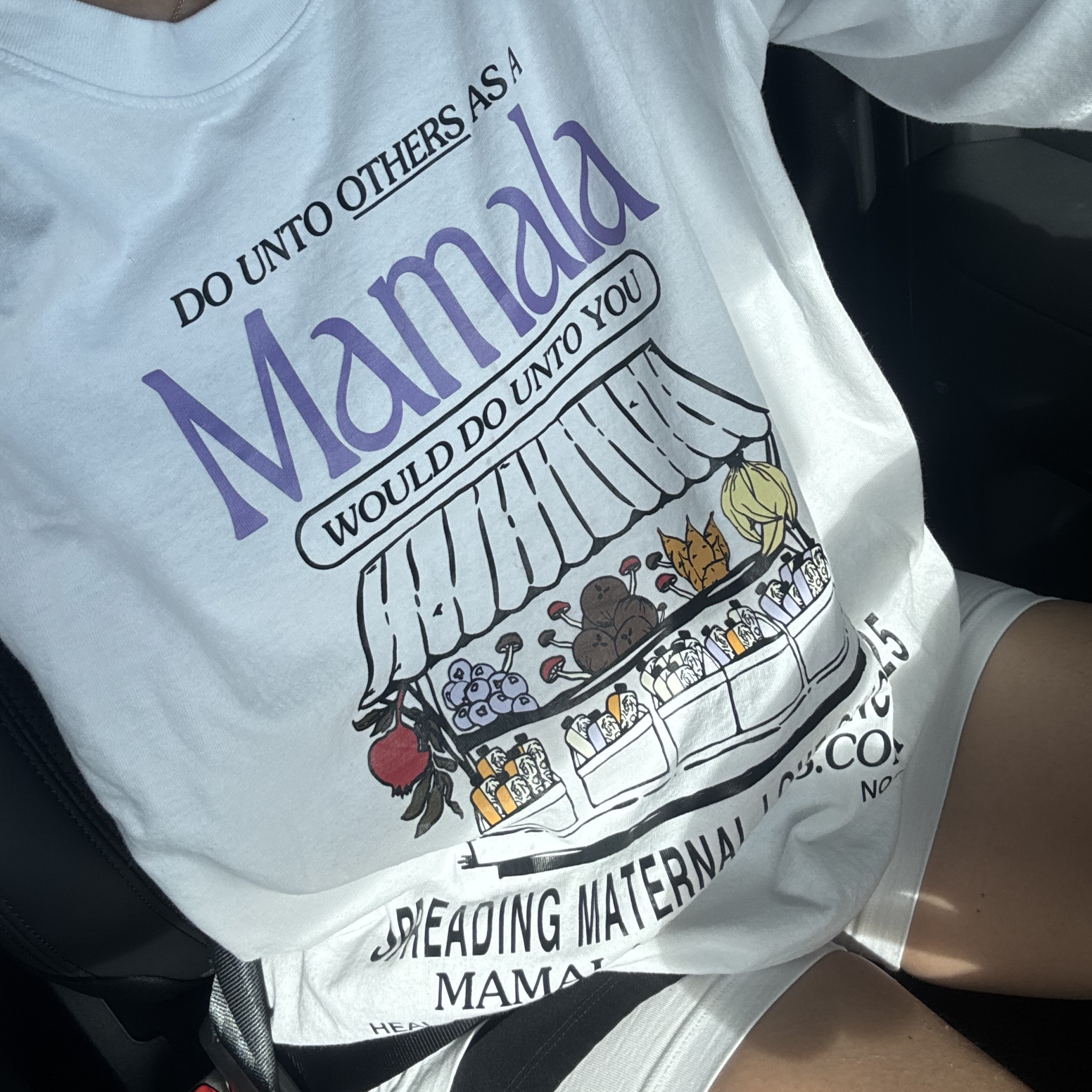 Person in a Mamala Organics Mamala Fruit Stand Long Sleeve, featuring colorful art, seated in a car.