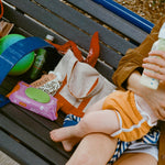 Person holding a baby on a bench with snacks and a bottle