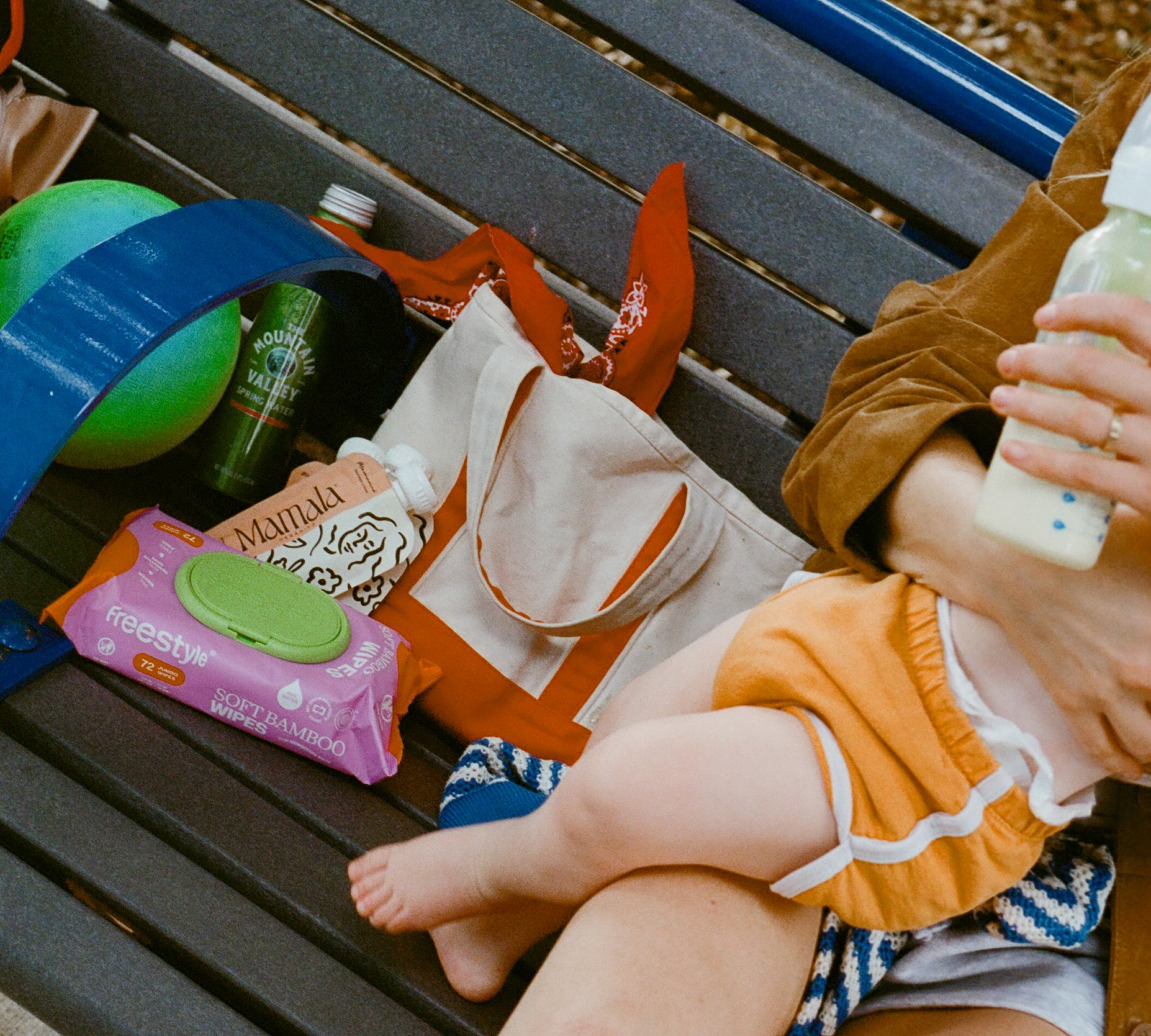 Person holding a baby on a bench with snacks and a bottle