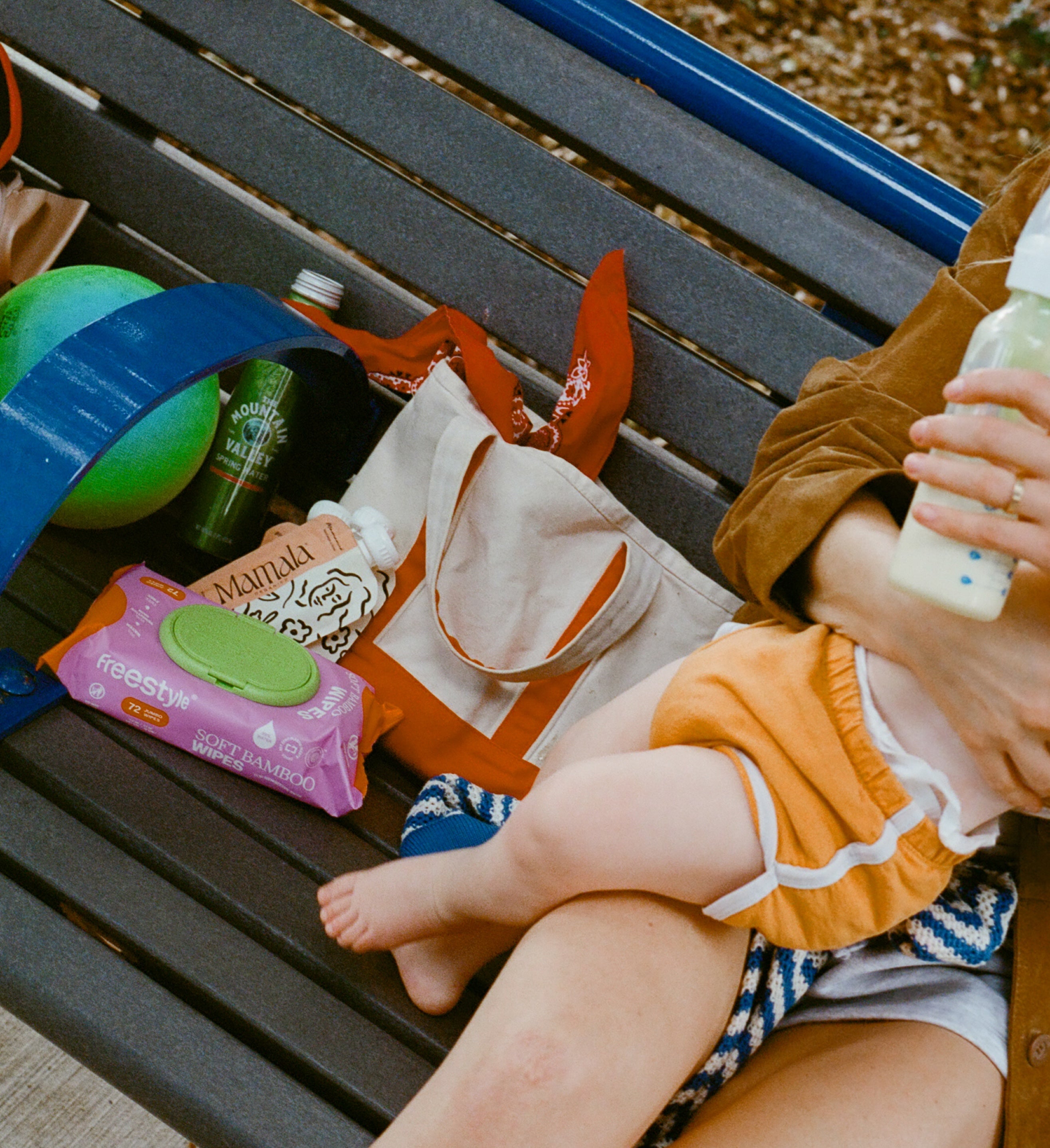 Person holding a baby on a bench with snacks and a bottle