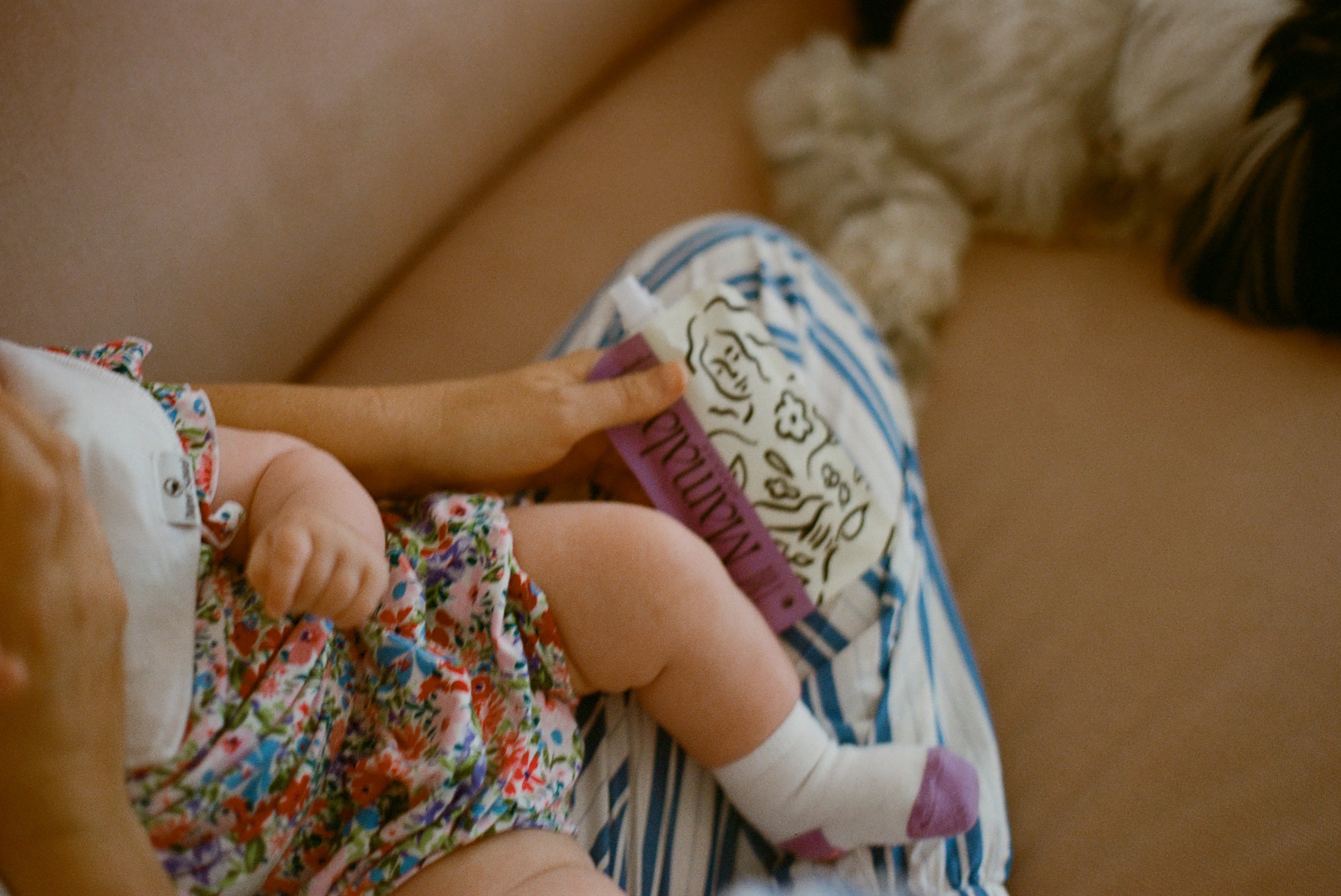 Baby in floral bloomers sitting on a person's lap with a dog in the background and a hand holding a Mamala Organics pouch.