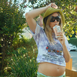 Woman in a green hat and sunglasses sips a drink, wearing the Mamala x La Bananita Tee by Mamala Organics and green shorts.